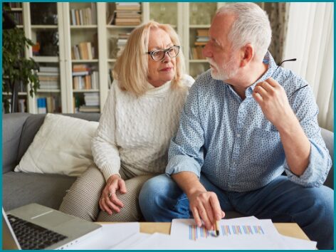 un couple de retraités discute vivement en consultant des documents et graphiques sur une table